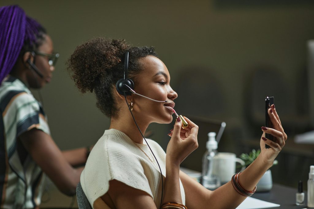 pexels photo 7689746 7689746 Two women multitasking in a call center, using headsets while applying makeup. Modern office life.
